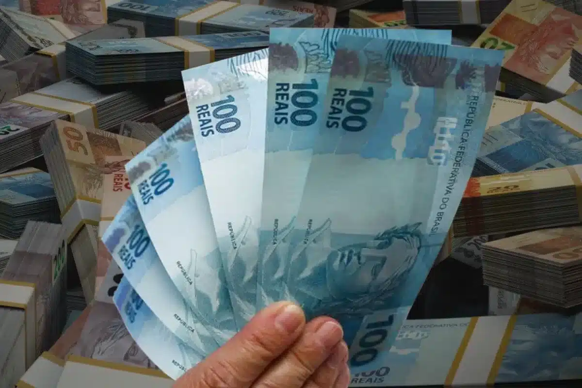 Mão segurando notas de R$ 100 para ilustrar adicional de R$ 1.486 no salário referente ao Abono Salarial PIS/Pasep.