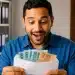 Trabalhador brasileiro surpreso segurando envelope com notas de reais, representando o adicional de R$ 1.486 no salário.