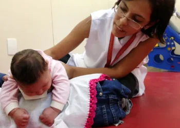 Profissional da saúde realiza atendimento em uma criança pequena em ambiente de reabilitação, exemplo do trabalho desenvolvido em áreas como Fisioterapia e Terapia Ocupacional.