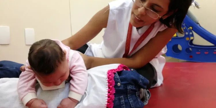 Profissional da saúde realiza atendimento em uma criança pequena em ambiente de reabilitação, exemplo do trabalho desenvolvido em áreas como Fisioterapia e Terapia Ocupacional.