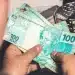 Pessoa segurando notas de 100 reais simbolizando possível aumento do BPC/INSS.