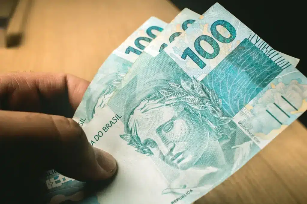 Notas de cem reais representando o valor projetado do BPC atrelado ao salário mínimo no Brasil
