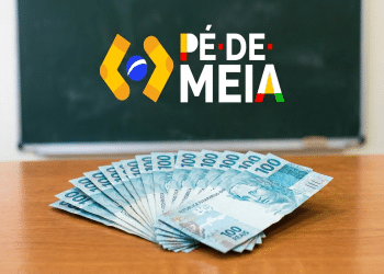 Notas de R$ 100 em leque sobre mesa com logotipo Pé-de-Meia e lousa verde ao fundo, simbolizando as datas de pagamento neste mês de maio.