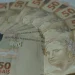 Leque de cédulas de cinquenta reais espalhadas sobre superfície clara em close que destaca o dinheiro em espécie