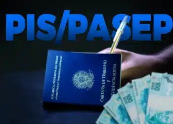 Carteira de Trabalho azul com cédulas de cem reais ao lado de cartão do PIS Pasep da Caixa sobre mesa de madeira