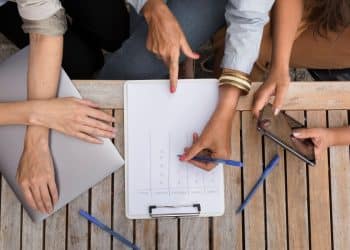 Grupo de pessoas analisando gráfico em prancheta durante reunião sobre jornada de trabalho.