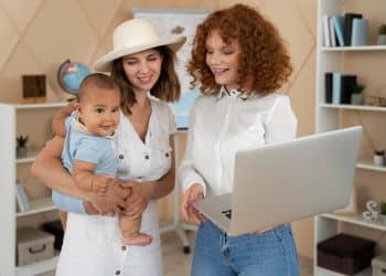 Mãe com bebê no colo conversa com consultora de carreira que mostra oportunidades de trabalho flexível em um notebook