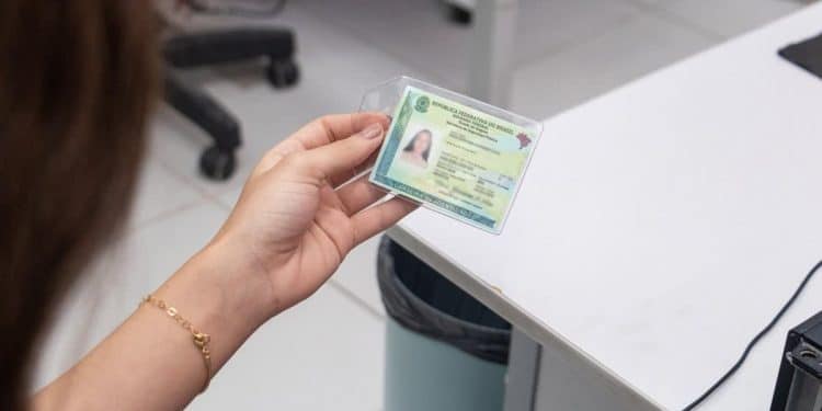 Mulher segura a nova Carteira de Identidade Nacional plastificada sobre balcão de atendimento em ambiente de repartição pública