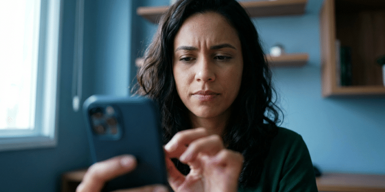 Mulher observa a tela do celular com expressão concentrada, sentada em ambiente interno