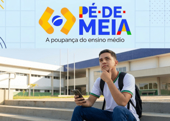 Estudante do ensino médio consulta o celular em frente a uma escola pública, com a logomarca do Pé-de-Meia