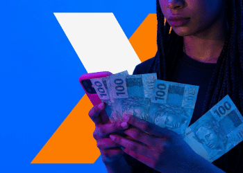 Mulher segura cédulas de R$ 100 e celular durante consulta ao aplicativo da Caixa