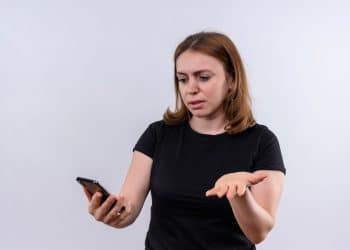 Mulher de camiseta preta com expressão de surpresa enquanto observa a tela do celular