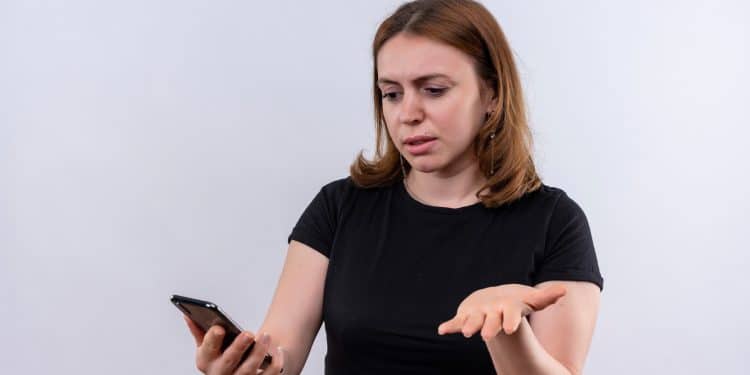Mulher de camiseta preta com expressão de surpresa enquanto observa a tela do celular
