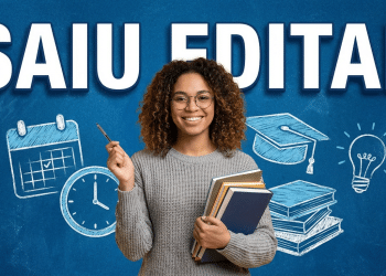 Jovem sorridente com cabelo cacheado, óculos e suéter cinza segura livros e caneta com texto "Saiu Edital" ao fundo.