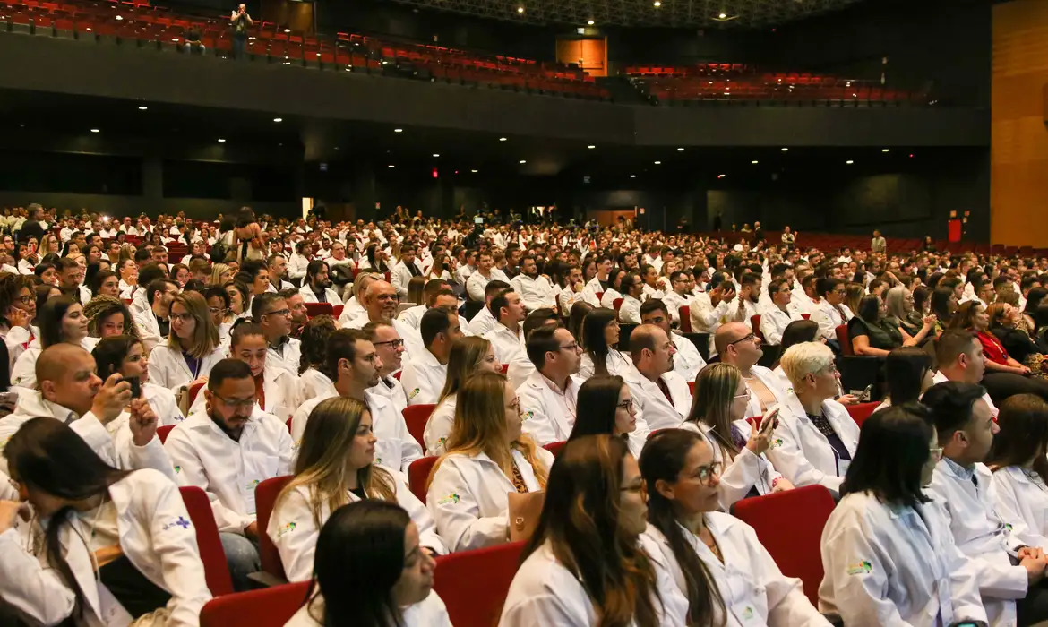 Plateia com dezenas de médicos de jaleco branco reunidos em um auditório, em referência ao mercado de trabalho da Medicina no Brasil.