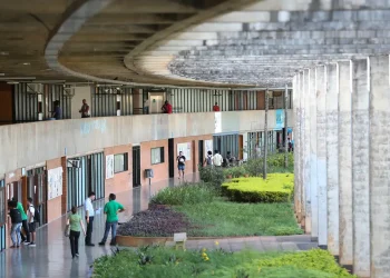 Vista do corredor de um campus universitário com estudantes caminhando entre os blocos de salas de aula, ilustrando a lista de cursos com pouca leitura no ensino superior