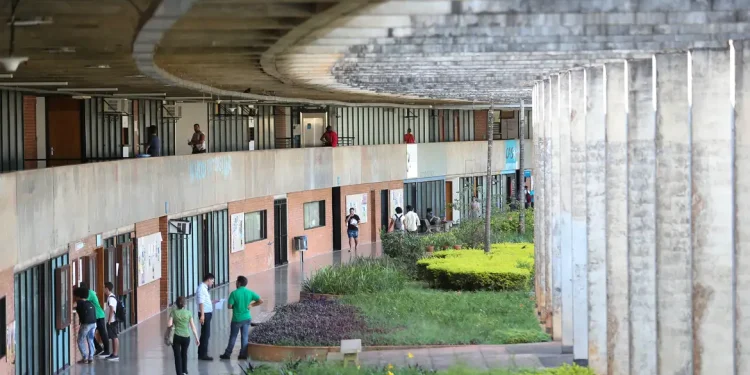 Vista do corredor de um campus universitário com estudantes caminhando entre os blocos de salas de aula, ilustrando a lista de cursos com pouca leitura no ensino superior