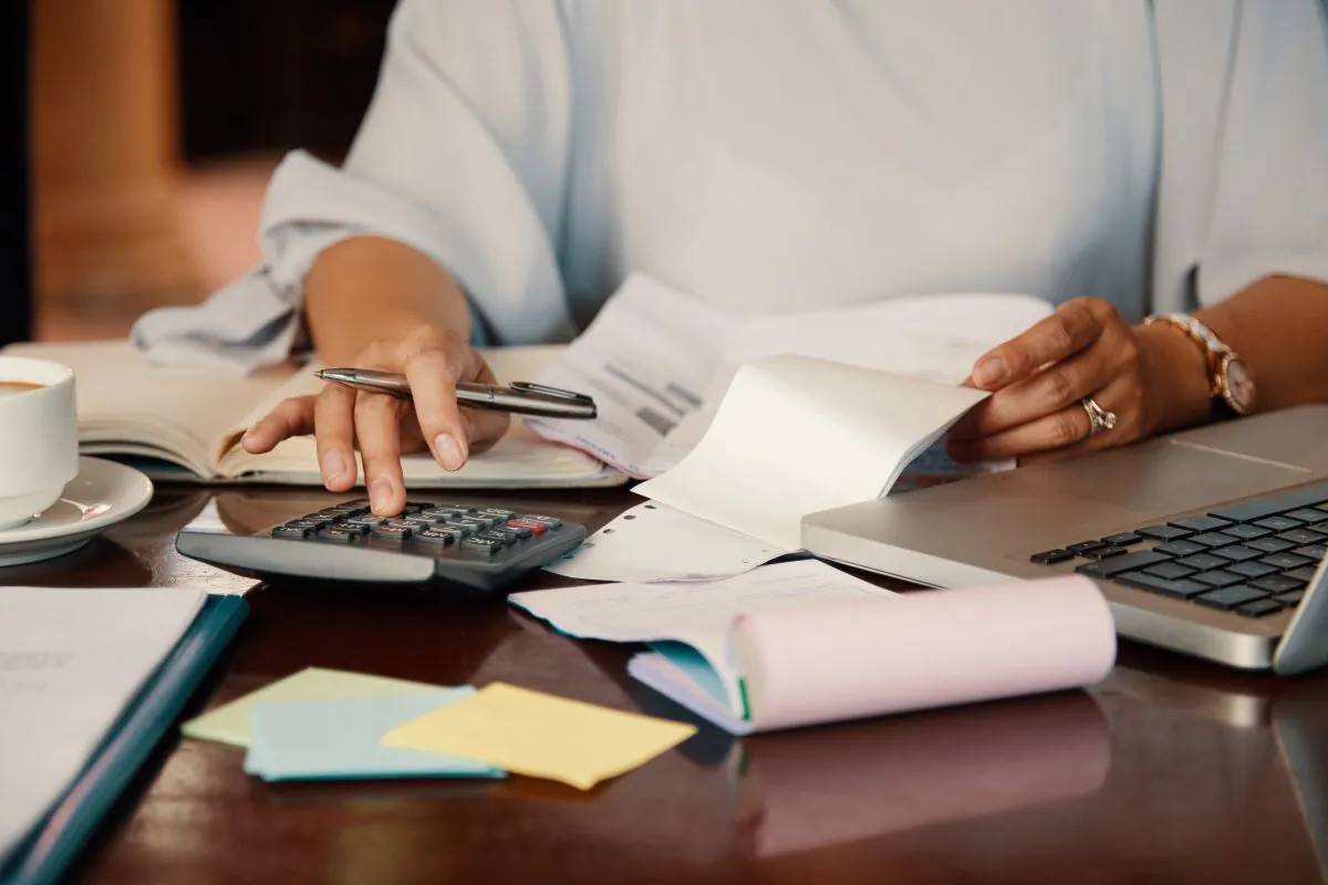 Mulher fazendo contas com calculadora, boletos e notebook sobre a mesa, em referência à organização das dívidas para renegociação dentro do Novo Desenrola Brasil 2026.