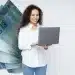 Profissional sorridente trabalhando com notebook ao lado de cédulas de R$ 100, em referência aos altos salários da carreira de desenvolvedor de inteligência artificial em regime de trabalho remoto.