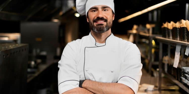 Chef de cozinha com uniforme branco e braços cruzados em cozinha