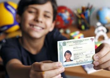 Adolescente sorri e mostra a Carteira de Identidade Nacional segurando o documento com as duas mãos.