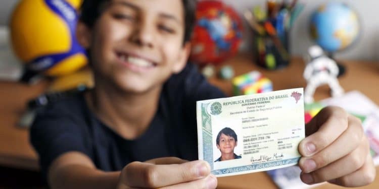 Adolescente sorri e mostra a Carteira de Identidade Nacional segurando o documento com as duas mãos.