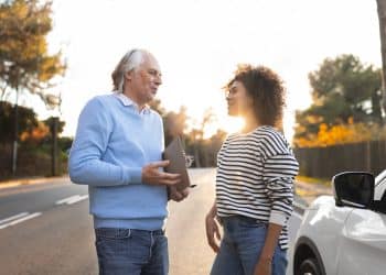 Homem mais velho e mulher jovem conversam de forma tranquila e sorridente ao lado de um carro, ilustrando os traços de personalidade de quem agradece no trânsito segundo especialistas