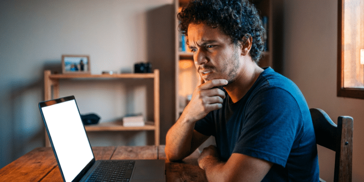 Homem observa a tela do notebook com expressão de dúvida