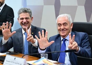 Dois senadores em comissão do Senado Federal sorrindo e mostrando os dedos das mãos representando o número cinco e o número dois