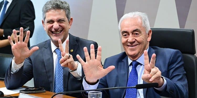 Dois senadores em comissão do Senado Federal sorrindo e mostrando os dedos das mãos representando o número cinco e o número dois