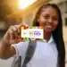 Estudante do ensino médio sorrindo segurando o cartão do Pé-de-Meia, em referência aos critérios de exclusão do programa em 2026