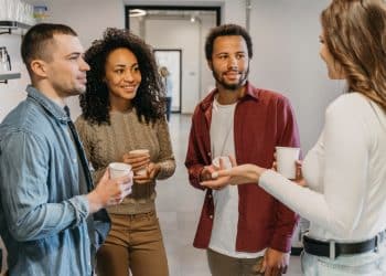 Grupo de quatro pessoas conversando e sorrindo em ambiente descontraído enquanto seguram copos de café