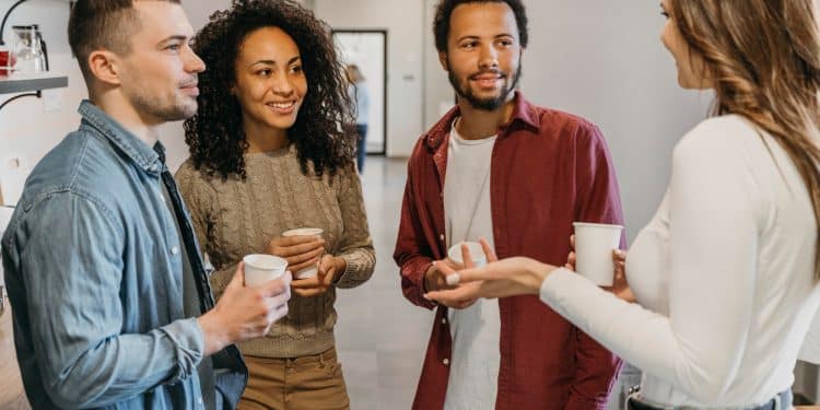 Grupo de quatro pessoas conversando e sorrindo em ambiente descontraído enquanto seguram copos de café