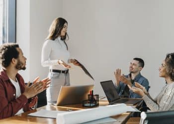 Profissional apresenta ideia em reunião e recebe aplausos de colegas, exemplo de comunicação eficaz no trabalho