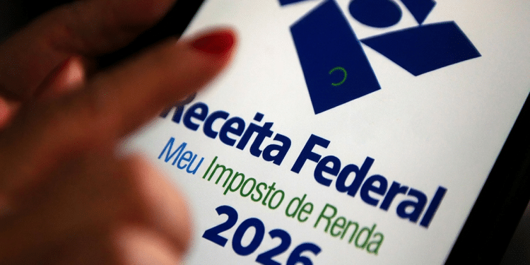 Mão com unhas vermelhas apontando para tela do celular exibindo logo da Receita Federal e Meu Imposto de Renda 2026.