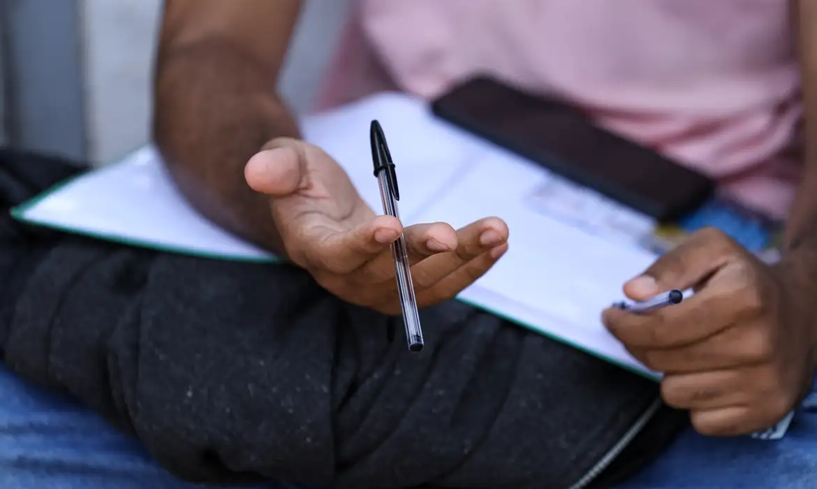 Jovem segura caneta e caderno enquanto se prepara para confirmar a inscrição automática no Enem 2026