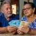 Aposentados conferindo notas de reais em casa, representando os pagamentos do INSS de maio para quem recebe antes e para quem recebe mais.