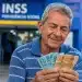 Aposentado segura cédulas de real em frente a uma agência do INSS, representando o pagamento de R$ 2.431,50 ou menos na próxima semana.