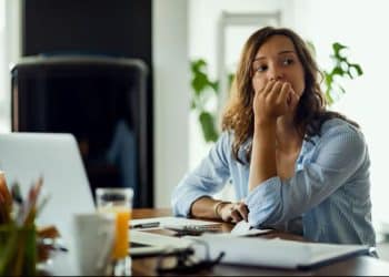 Mulher pensativa sentada em frente ao notebook