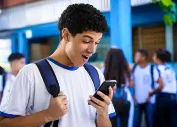 Estudante do ensino médio consultando no celular o benefício do Pé-de-Meia, representando a gratuidade no Enem 2026 e o incentivo extra de R$ 200.