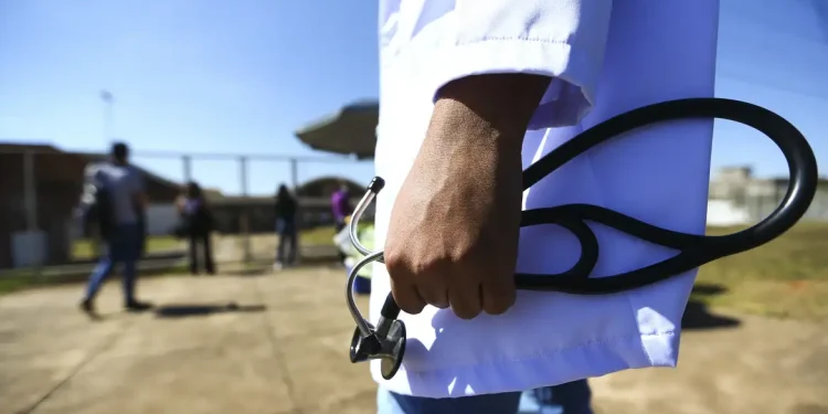 Médico de jaleco branco segurando um estetoscópio ao ar livre, em referência às vantagens de seguir a carreira de Medicina.