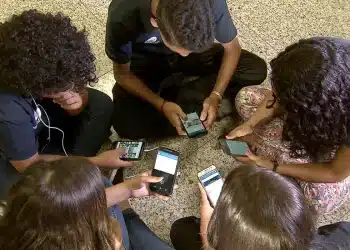 Grupo de adolescentes sentados em roda mexe em celulares, cena que ilustra o público afetado pela nova classificação indicativa do YouTube
