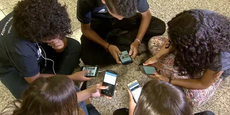 Grupo de adolescentes sentados em roda mexe em celulares, cena que ilustra o público afetado pela nova classificação indicativa do YouTube