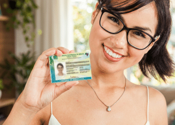 Mulher de óculos sorri e segura a Carteira de Identidade Nacional próxima ao rosto.