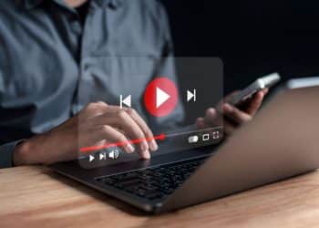 Pessoa assiste vídeo do YouTube no notebook enquanto segura o celular.