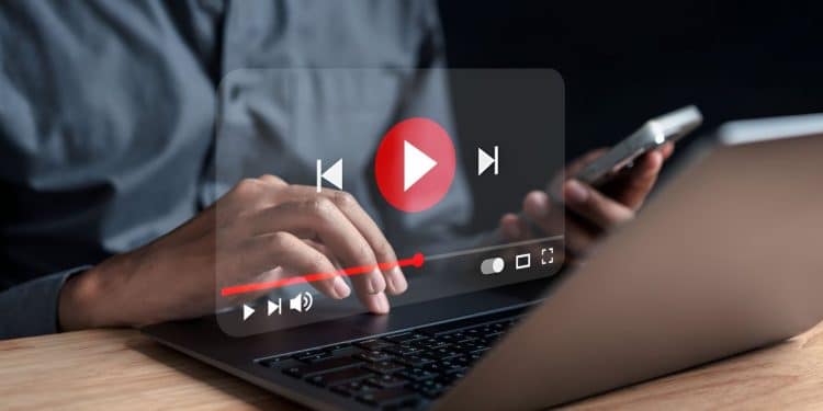 Pessoa assiste vídeo do YouTube no notebook enquanto segura o celular.