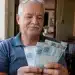 Aposentado brasileiro segura notas de R$ 100 em casa, representando o pagamento para quem recebe acima do salário mínimo a partir de 1º de junho.