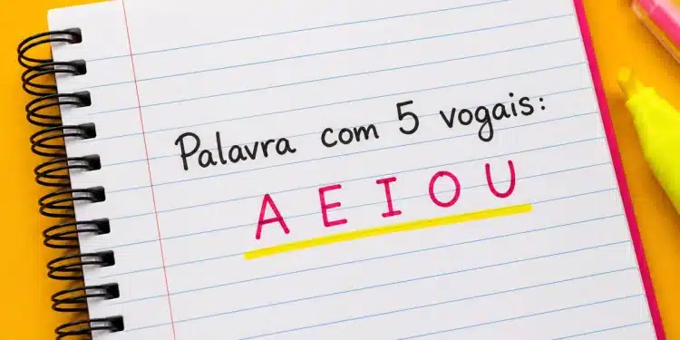 Caderno espiral aberto com a frase “Palavra com 5 vogais: A E I O U” escrita em destaque colorido sobre fundo amarelo vibrante.