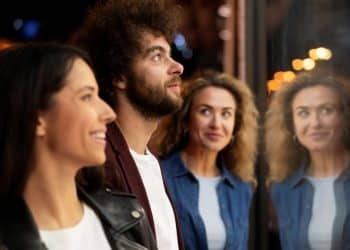 Homem e duas mulheres observam algo enquanto conversam próximos a uma vitrine iluminada à noite