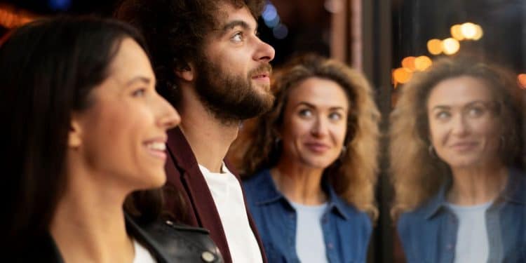 Homem e duas mulheres observam algo enquanto conversam próximos a uma vitrine iluminada à noite